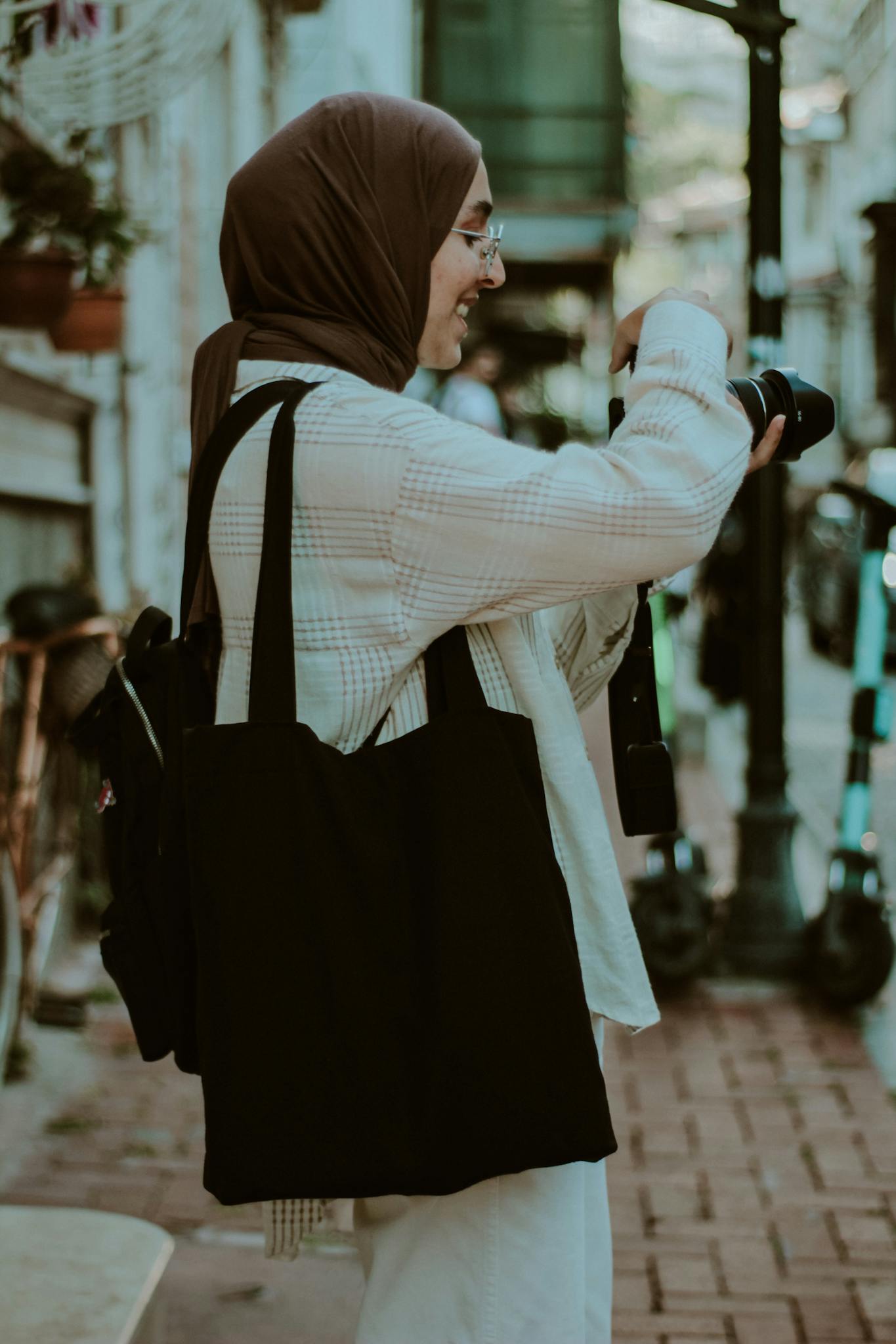 A smiling Muslim woman with a hijab takes photos on a street in İstanbul, Türkiye.